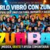 Gran grupo de vecinos y bailarines posando felices con un cartel de ZUMBA en el escenario del Teatro Municipal durante el Festival de Ritmos en Merlo.